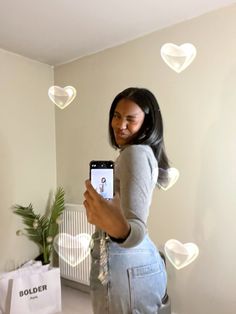 a woman taking a selfie with her cell phone in front of hearts floating from the ceiling