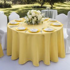 the table is set with white and yellow plates, napkins, and flower centerpieces