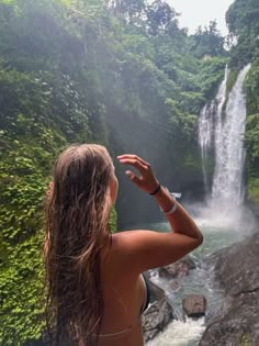 a woman standing in front of a waterfall looking up at the water from her back