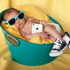 a baby wearing sunglasses and headphones laying in a blue bucket with an ipod on it