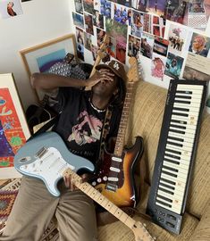 a man sitting on top of a couch with an electric guitar next to him in front of a keyboard