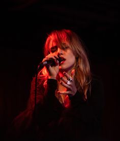 a woman singing into a microphone on stage with red light coming from her mouth and hands