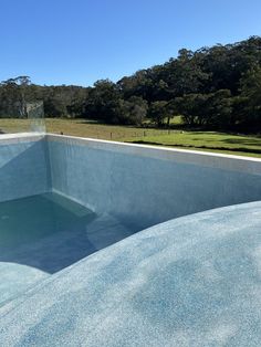 an empty swimming pool in the middle of a grassy area with trees and blue sky