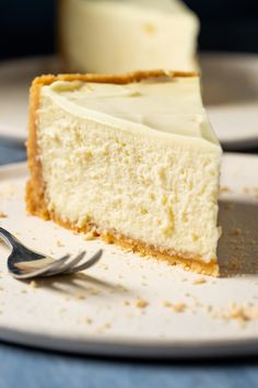 a piece of cheesecake on a white plate with a fork and blue table cloth