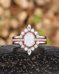 a white opal and diamond ring on top of a black piece of wood with rocks in the background