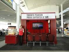 a woman standing in front of a red booth at an airport with a television on it