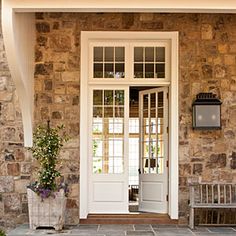 the front door is open and there are flowers in pots on the stone steps outside