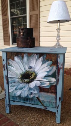 a painted side table with a white flower on it and a lamp next to it