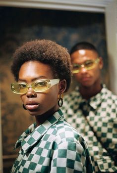 two people wearing sunglasses and checkered shirts in front of a mirror with one person looking at the camera