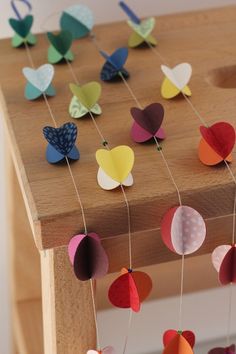 colorful paper butterflies hanging from clothes pins on a wooden board with string attached to them