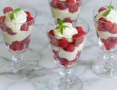 a dessert with strawberries and whipped cream in a glass on a white table next to a spoon