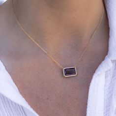 a woman wearing a gold necklace with an amethyst stone