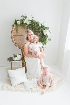 a mother and her two babies sitting on a chair in front of a floral wreath