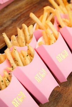 pink boxes filled with french fries sitting on top of a wooden table next to each other