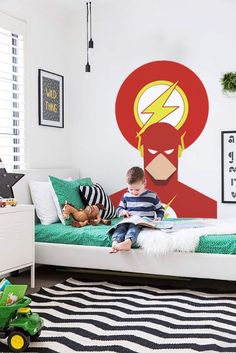 a young boy sitting on top of a bed in front of a wall mural with the flash