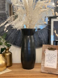 a black vase with white flowers in it on a table next to two gold vases