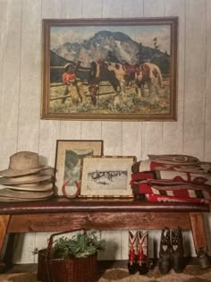 a painting hanging on the wall above a wooden bench with hats and other items sitting on it