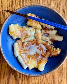 chopsticks sticking out of some food in a blue bowl on a wooden table