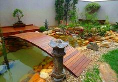 a wooden bridge over a small pond in a backyard with rocks and plants around it