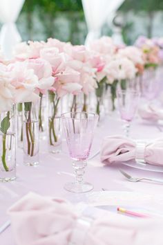 a long table with pink flowers in vases and place settings on the tablescloth