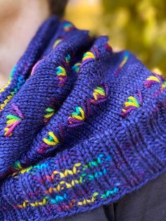 a person wearing a purple knitted scarf with multicolored flowers on it's edge