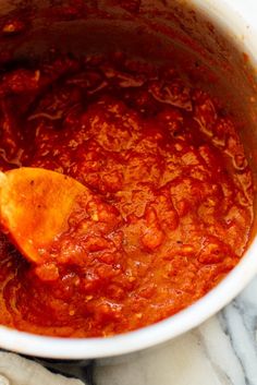 a wooden spoon in a white bowl filled with sauce on top of a marble counter