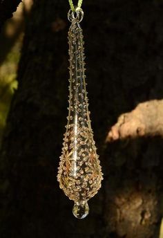 a glass hanging from a tree branch in the dark with beads and chains attached to it