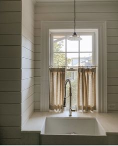 a kitchen sink sitting under a window next to a window sill with curtains on it