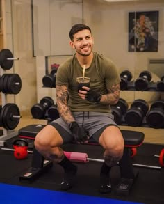 a man sitting on top of a bench in a gym holding a drink and looking at the camera