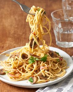 someone is eating spaghetti with meat and vegetables on a plate next to a glass of water