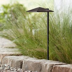 an outdoor lamp in the middle of some rocks and grass next to a rock wall