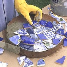 a person in yellow gloves is cutting up blue and white tiles on a wooden table