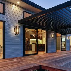 a wooden deck with lights on it next to a blue building and water in the foreground