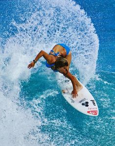 a woman riding a surfboard on top of a wave in the ocean with blue water