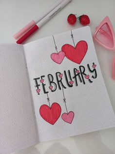 an open notebook with the word february written on it and two hearts hanging from strings