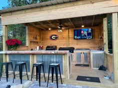 an outdoor bar with three stools and a television on the wall behind it,