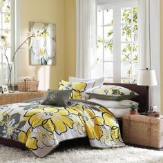 a bedroom with yellow and white bedding, windows, rugs and pillows on the floor