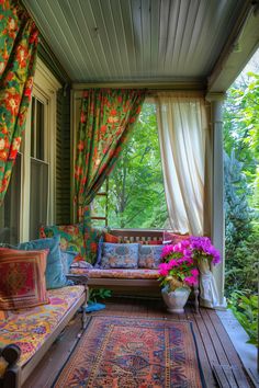 a covered porch with couches, rugs and flowers on the floor next to it