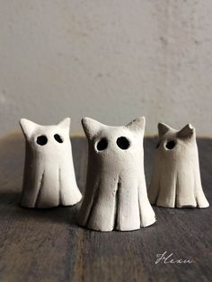 three small white ceramic cats sitting on top of a wooden table next to each other