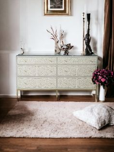 a white and gold dresser with flowers on top in a living room next to a window