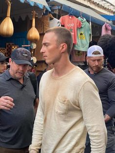 a group of men standing around each other in front of a building with lots of hanging items