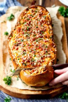 a person cutting into a cheesy bread dish on top of a wooden board