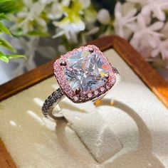 a fancy ring with pink and white diamonds sits in a wooden box next to flowers