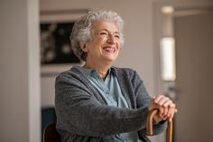 an older woman sitting in a chair with her hands on the handlebars and smiling