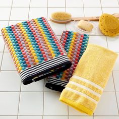 three towels and two combs on a white tiled floor next to a yellow toothbrush