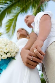 a bride and groom holding hands with palm trees in the backgroung behind them