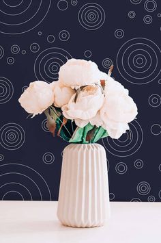 a white vase filled with flowers on top of a table next to a blue wall