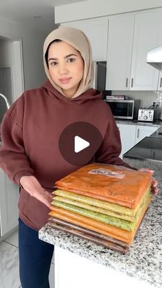 a woman in a hijab is holding a stack of food on a counter