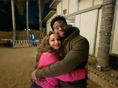 a man and woman hugging each other in front of a building