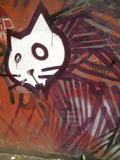 graffiti on the side of a wall with a white cat face and purple palm leaves